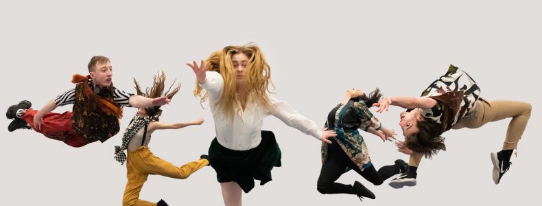 Five dancers in brightly coloured costumed leap in the air at different angles against a plain white backdrop.